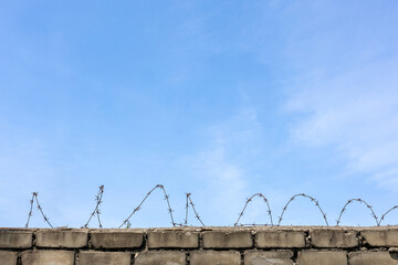 Barbed wire on top of concrete wall under blue sky. Outdoor surveillance and protection structure....
