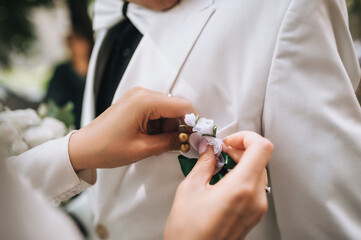 Bride attaches flower boutonniere to groom's suit jacket by hand during wedding ceremony. Wedding...