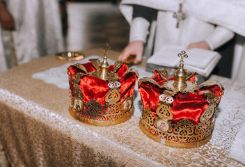 Two beautiful Christian crowns made of red fabric, with a gold frame, a pattern, and a cross lie on...