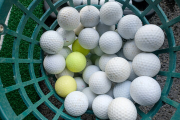 Top view of a basket filled with white and yellow golf balls with slight usage marks, placed inside a green plastic basket. Perfect for illustrating sports, training