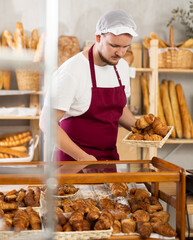 Young man seller stands at Spanish bakery counter with basket filled fresh croissants. Employee...
