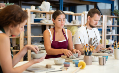 Three students in pottery workshop learn to create homemade plates and other utensils from clay