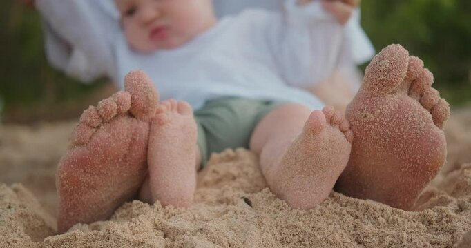 Close up of baby and mothers feet sitting on the beach on the sand and relaxing. Family vacation by the ocean on the beach in the tropics. Baby first steps on the sand. Mothers Day. - Powered by Adobe