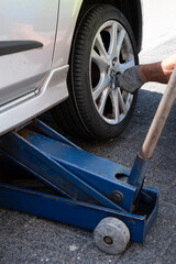 Silver-gray car stands on a hydraulic jack. Mechanic installs the rim with a new tire in a street....