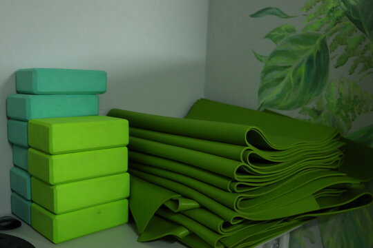 A collection of vibrant green yoga mats and blocks is organized on a shelf in a serene studio. The calming decor enhances the peaceful atmosphere ideal for practice.