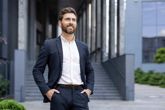 A confident businessman smiles while standing outdoors near a modern office building, hands in pockets.
