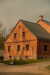 A well-preserved historic red brick building with a gabled roof, photographed in soft evening light. The building features stone foundation walls.