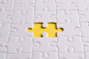 White puzzle with missing piece on yellow background, closeup