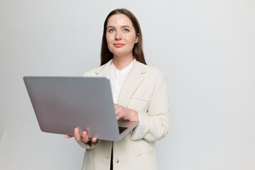 Young professional woman engages with laptop while standing against a neutral backdrop, showcasing confidence 