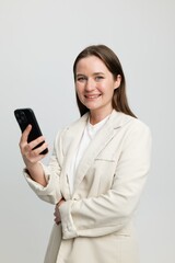 Cheerful professional woman holding smartphone, bright studio setting, engaging with technology, showcasing confidence and approachability