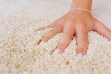 a woman's hand touching the beige Interior pile carpet made of polypropylene.