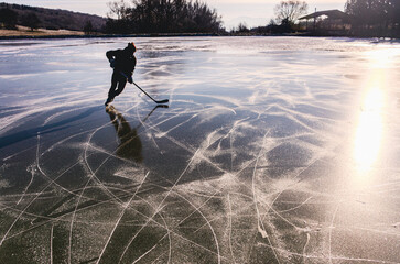 A man is skating on a frozen lake and is holding a hockey stick