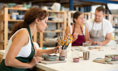 Woman learns to make designs on clay plate using brush and paint in a pottery workshop