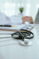 A professional in a white coat writes on a clipboard while using a laptop, suggesting healthcare administration, medical documentation, or online consultation.