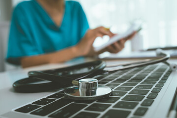 A female doctor sits at a desk in a clinic, reviews medical documents and uses a laptop during a consultation with a patient, representing professionalism and expertise in healthcare.
