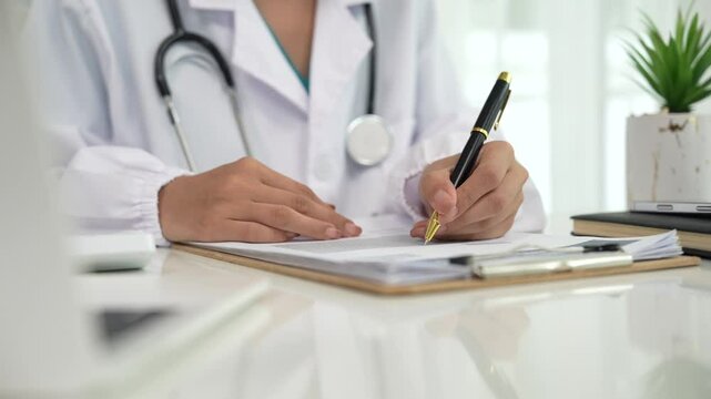 A professional in a white coat writes on a clipboard while using a laptop, suggesting healthcare administration, medical documentation, or online consultation.