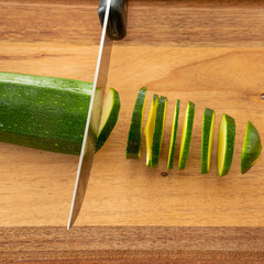 Cucumber is being cut with a knife, with the slices still standing upright on the cutting board.