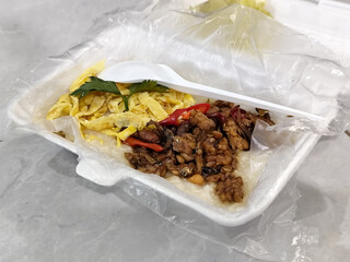 Chicken porridge served in a white styrofoam container covered with plastic, accompanied by sliced...