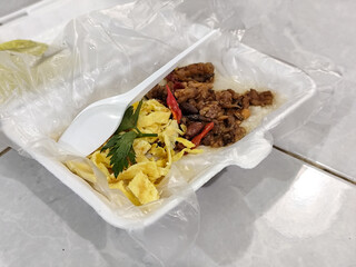 Chicken porridge served in a white styrofoam container covered with plastic, accompanied by sliced...