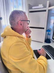 Handsome adult man sitting on desk looking at computer with worried expression.Man busy working on...