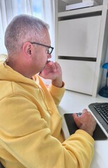Handsome adult man sitting on desk looking at computer with worried expression.Man busy working on...