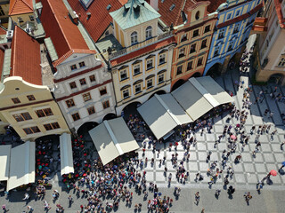 Large crowd of people are gathered in front of a building with a white roof. The crowd is spread out and some are standing under awnings. Prague. Czech Republic