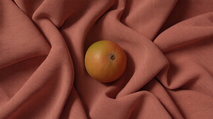 Single orange on draped terracotta fabric