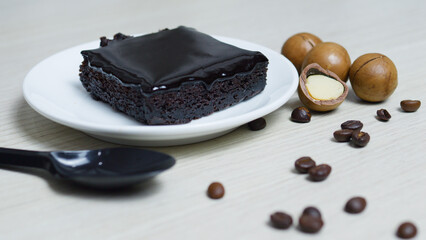 Rich chocolate brownie drizzled with dark ganache, resting on white plate, surrounded by roasted...