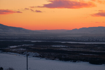 Ulan-Ude, Russia - Jan 31, 2023: Panoramic view from the height of the city and the Selenga River in winter against the background of the sunset sky.