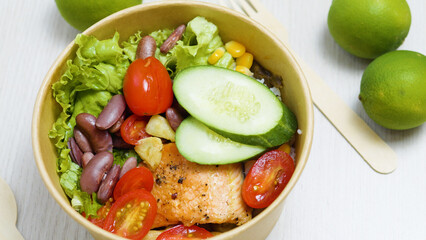 Cardboard bowl filled with a delicious and healthy salmon poke bowl, including rice, cucumber,...