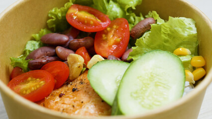 Grilled salmon nestled atop a vibrant salad featuring beans, cucumber, lettuce, tomato, and corn, creating a colorful and nutritious meal perfect for lunch or dinner