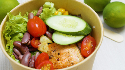 Grilled salmon salad with fresh cucumber, cherry tomatoes, beans, corn and lettuce served in an eco friendly paper bowl, promoting a healthy and sustainable lifestyle