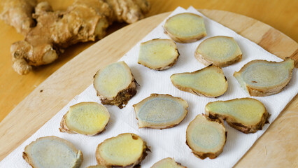 Thinly sliced pieces of blue ginger root are drying on a white paper towel on a wooden cutting board, showing the unique coloration and texture of the ginger