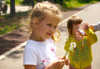 Pretty cute sisters having fun outdoors. Sisters walking at springtime enjoying nature, laughing. Baby girl taking a big gulps of water from a bottle, quenching thirst after activities. Happy family