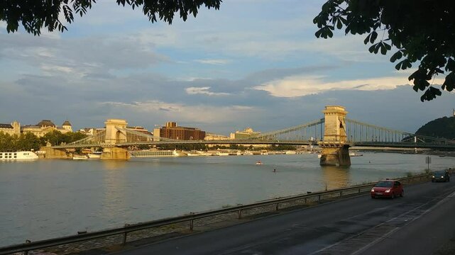 BUDAPESHT - JUL 21, 2019: Bridge over a river with a boat in the water. The bridge is green and has a lot of trees around it. Budapest, Hungary