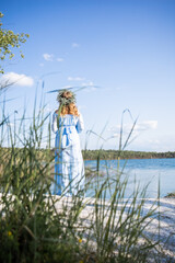 Woman standing on the edge of a lake. Woman in a blue dress and with a wreath on her head. Blue water, beautiful nature and view. Water nymph. Mavka