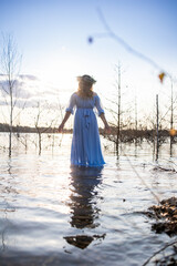 Water nymph. Lake and sunset. Woman standing in water. Woman in a blue dress and with a wreath on her head. Blue water, beautiful nature and view. Mavka