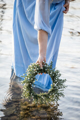 A woman places a wreath of flowers on the water. Water nymph. Lake and sunset. Woman in a blue dress. Mavka. Delicate female hands. 