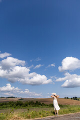 Young woman standing in a field. A magical landscape. White fluffy clouds in the sky. Woman in a hat and dress against a background of nature