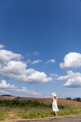 Young woman standing in a field. A magical landscape. White fluffy clouds in the sky. Woman in a hat and dress against a background of nature