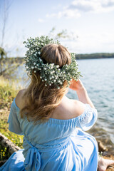 Woman sitting on the edge of a lake. Woman in a blue dress and with a wreath on her head. Blue water, beautiful nature and view. Water nymph. Mavka