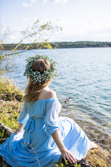 Woman sitting on the edge of a lake. Woman in a blue dress and with a wreath on her head. Blue water, beautiful nature and view. Water nymph. Mavka