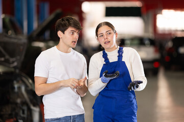 European guy consults with a car service worker about the repair and diagnostics of the car. Female...