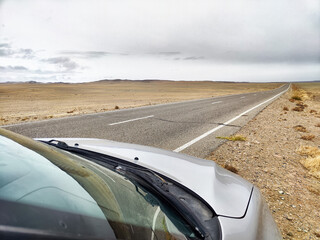 Road stretches endlessly through arid landscape under cloudy sky in remote area