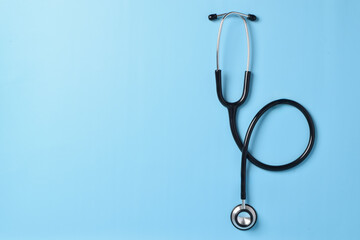 Black stethoscope isolated on a light blue background. Flat lay, top view. Space for text