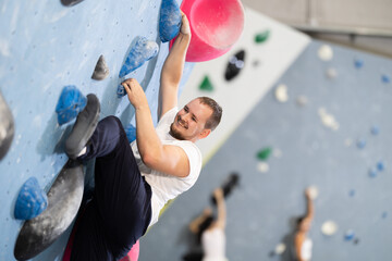 Man climbing a tall, indoor, man-made rock climbing wall