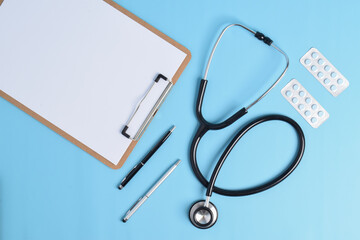 Stethoscope, blank clipboard and medicines on light blue background, top view. Cardiology and...