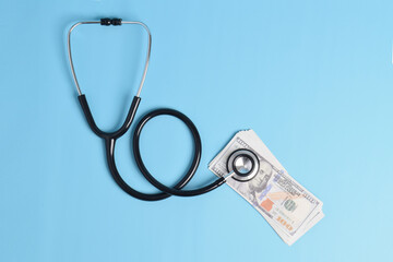 Black stethoscope and US dollar bills on light blue background, symbolizing medical costs, healthcare financing, and insurance expenses in the healthcare industry.