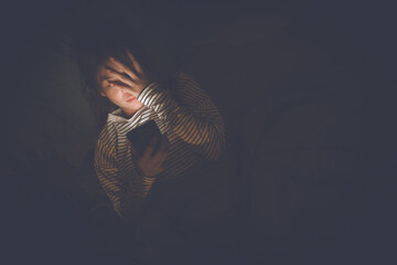 A young woman lies awake at night in bed, scrolling on her glowing phone, battling insomnia, loneliness, and digital addiction under soft light in a quiet room.