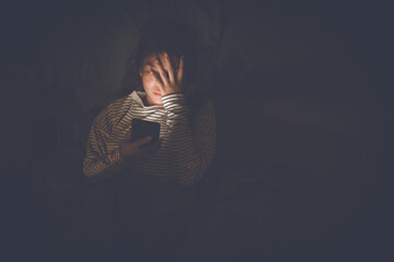 A young woman lies awake at night in bed, scrolling on her glowing phone, battling insomnia, loneliness, and digital addiction under soft light in a quiet room.